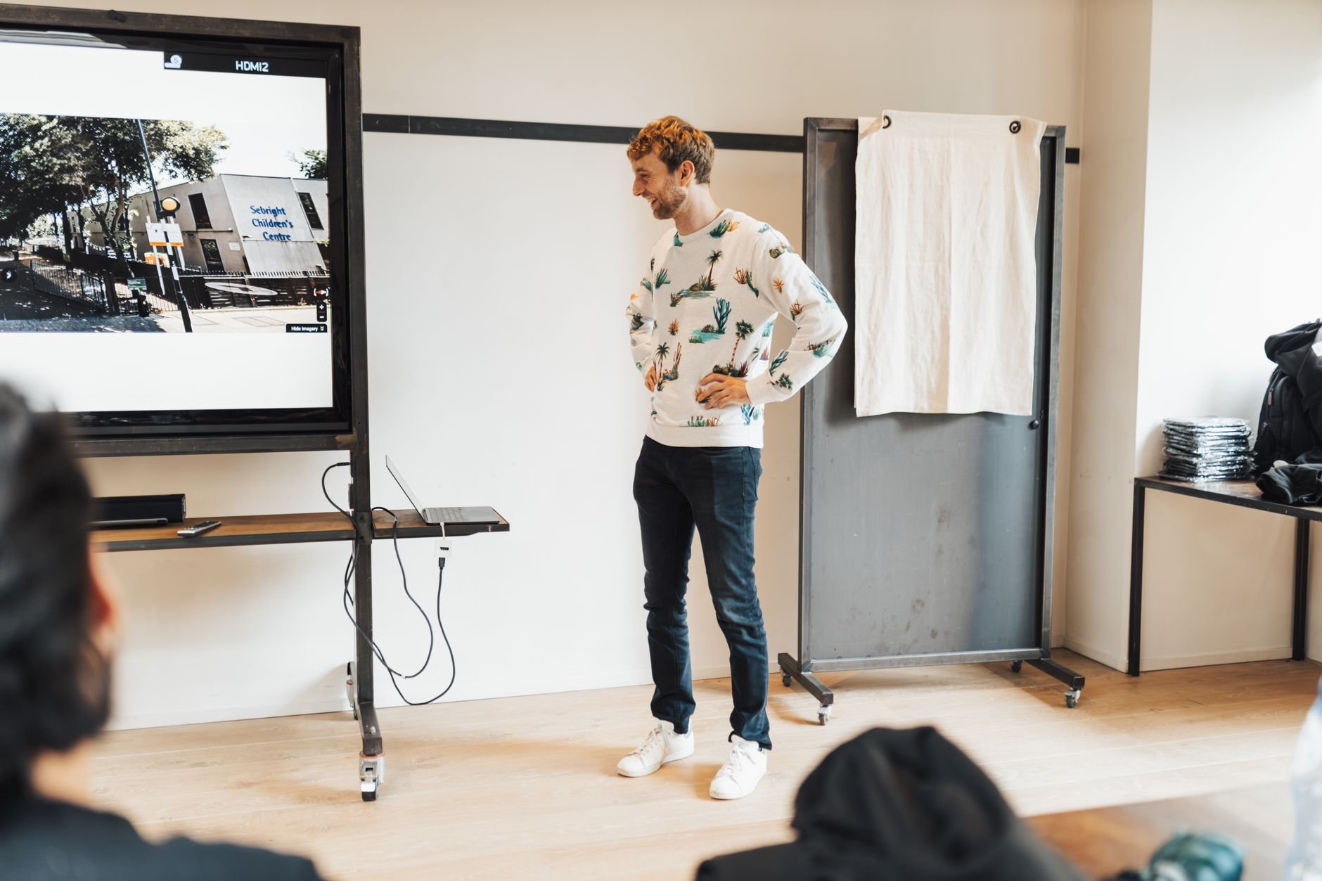 Man presenting on a large screen in a modern office setting, engaging an audience.